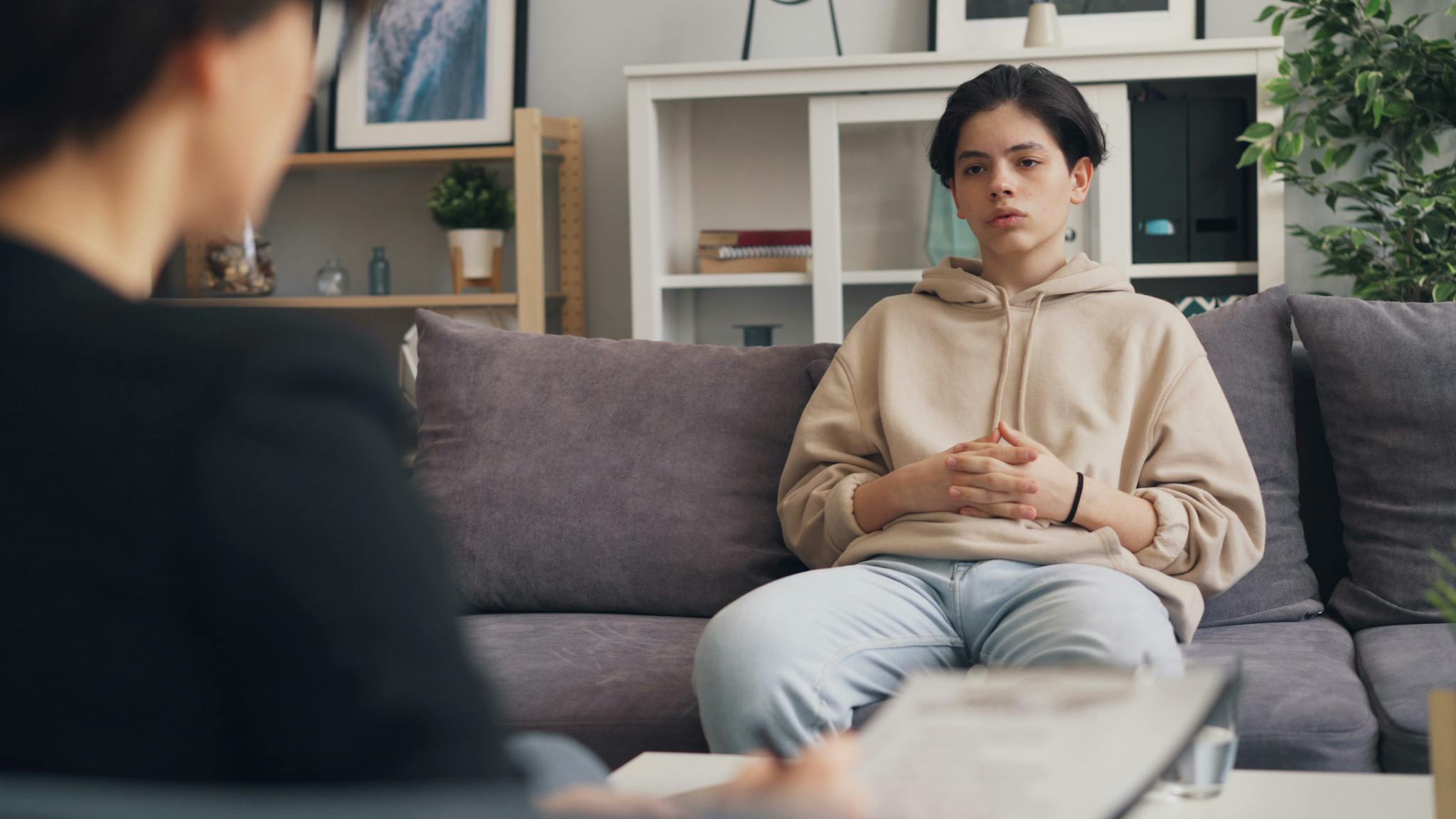 Calm teenager sitting on a sofa during a therapy session with a professional therapist.