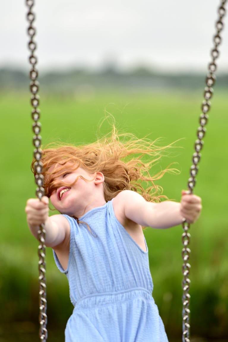A redhead girl enjoying a swing in a lush, green meadow on a sunny day, radiating happiness.