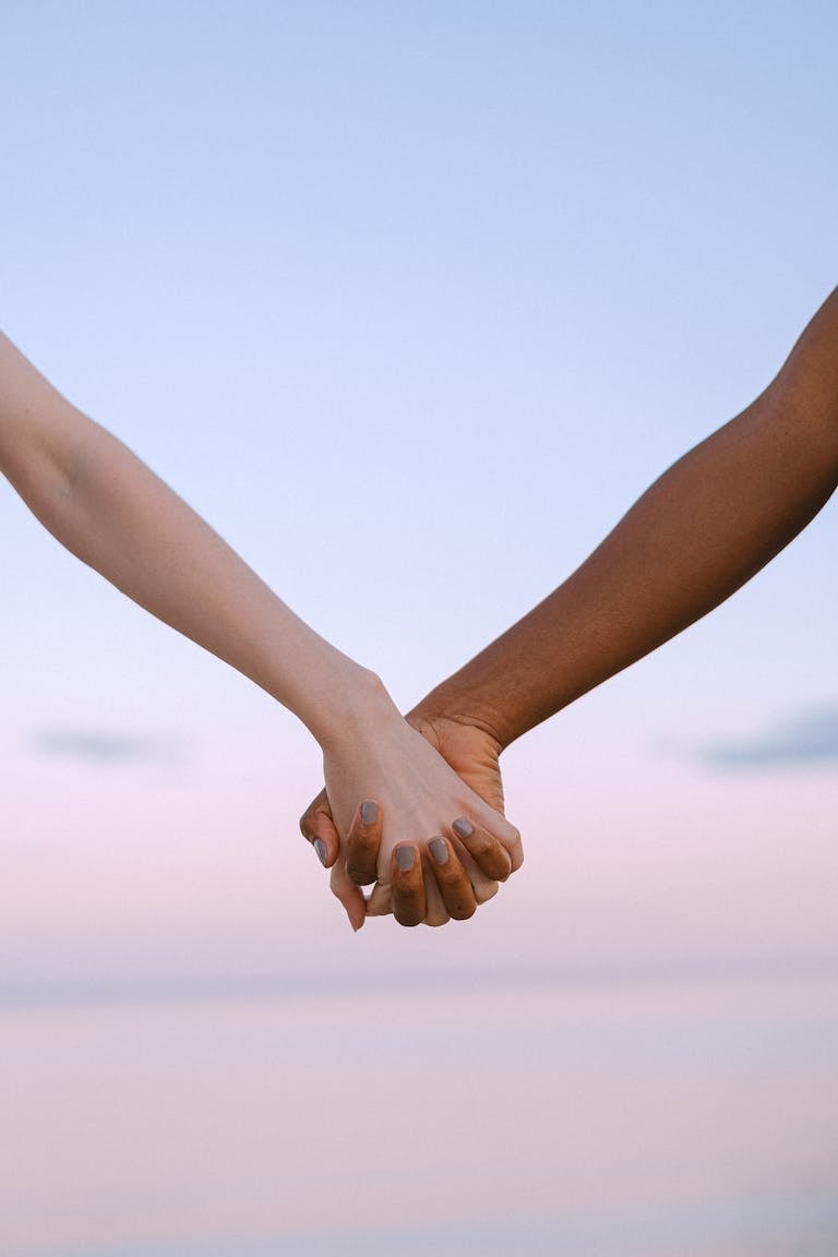 Closeup of multiracial hands holding, symbolizing unity and equality against a serene sky.