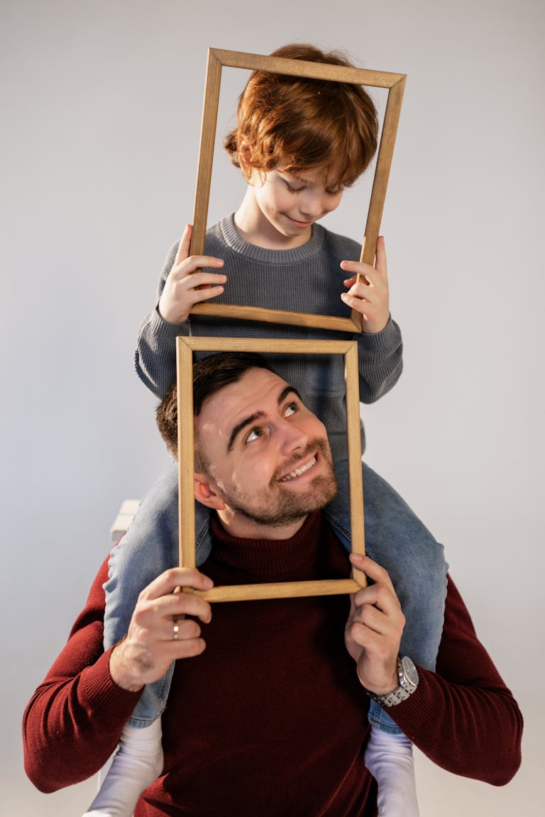 Father and son joyfully posing with wooden frames in a playful, intimate setting.