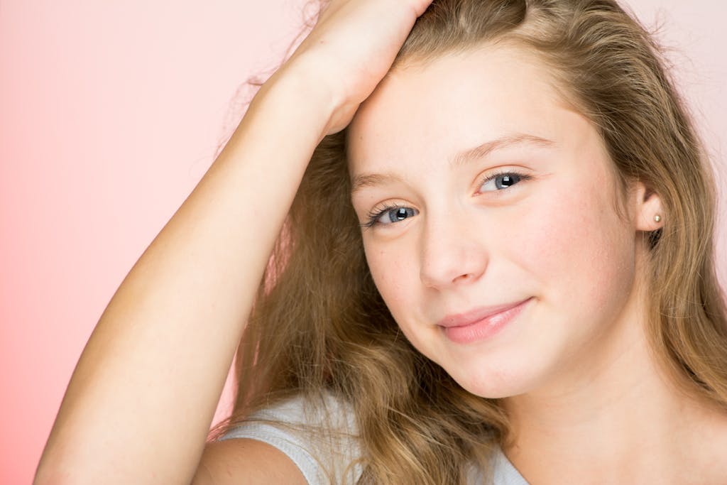 Portrait of a smiling teenage girl with blonde hair against a pink background, radiating positivity and warmth.