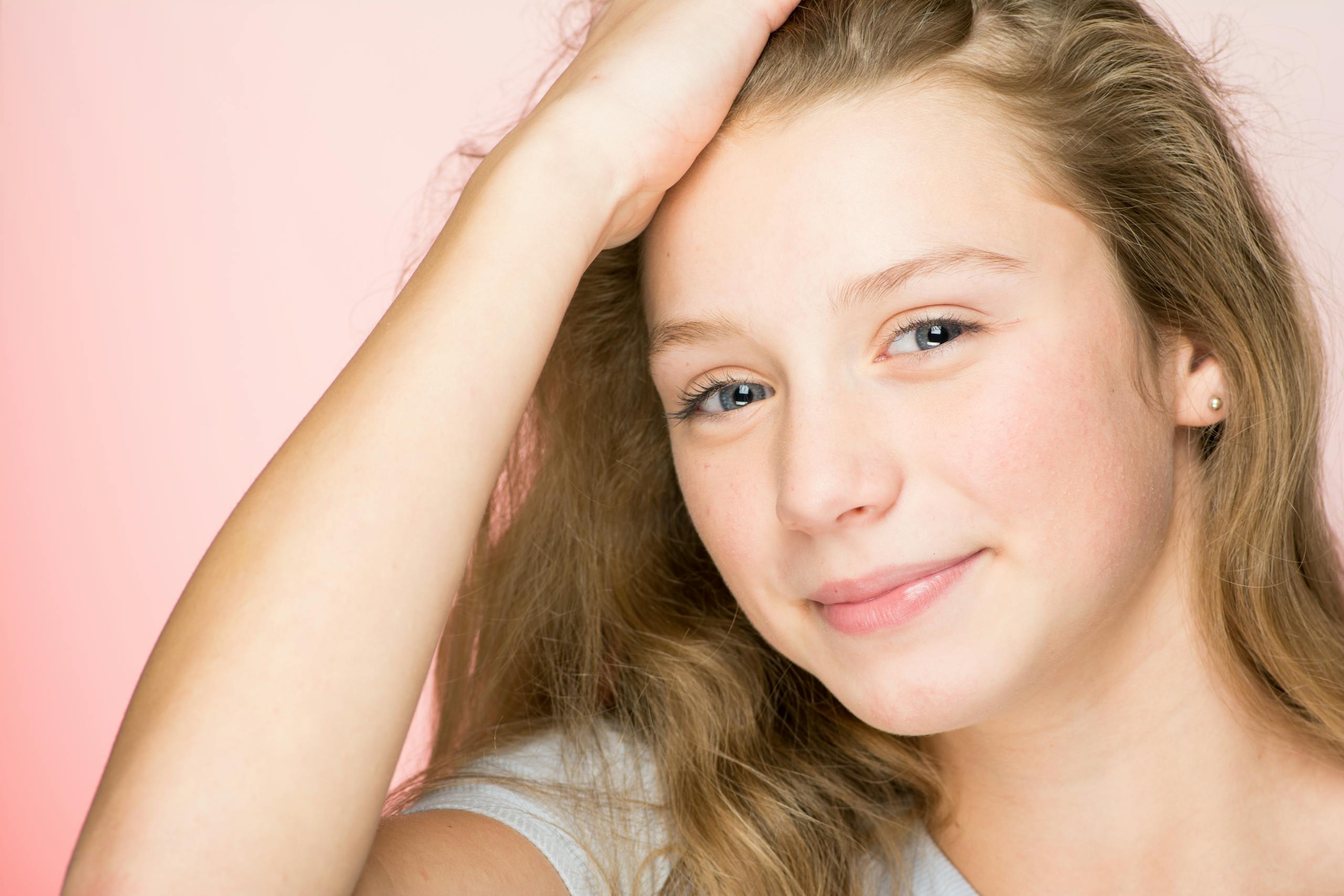 Portrait of a smiling teenage girl with blonde hair against a pink background, radiating positivity and warmth.